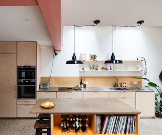 A ply kitchen designed to fit around appliances. There are hanging black pendant lamps and a floor with an industrial feel