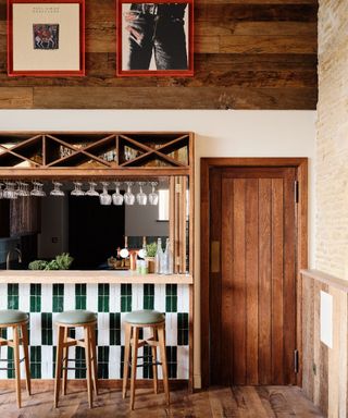 A log cabin kitchen with a breakfast bar decorated with white and green stripe tiles and wood paneling