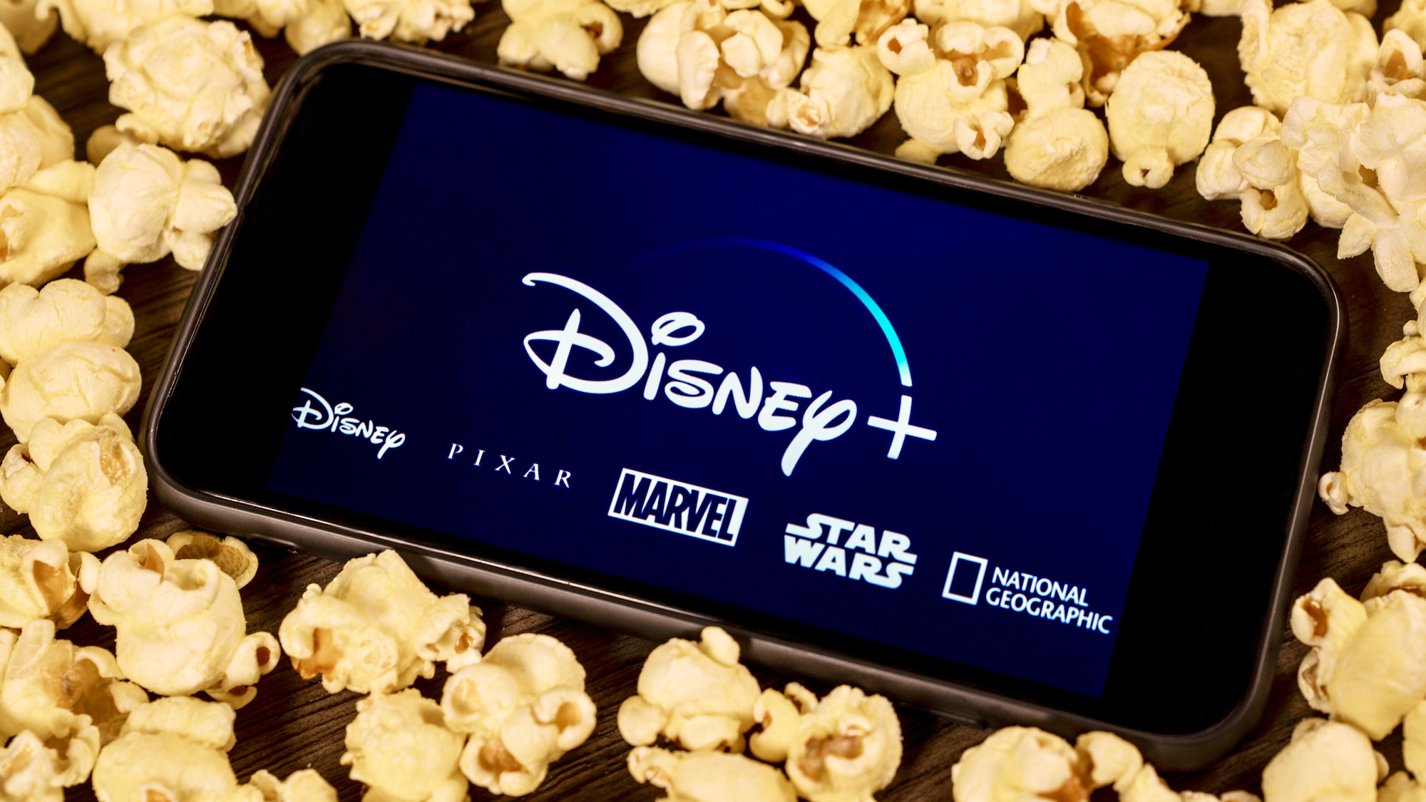 The Disney Plus logo on a phone surrounded by popcorn