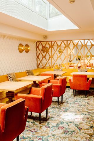 A warmly lit restaurant bar features inventive, plush furniture in orange, large plants, a mosaiced floor, and glass lighting.