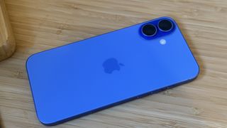 An ultramarine blue iPhone 16 on a wooden desk