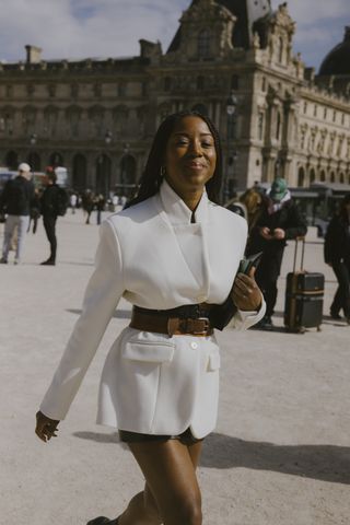 A guest a Paris Fashion Week wearing a white blazer with belts and black leather shorts