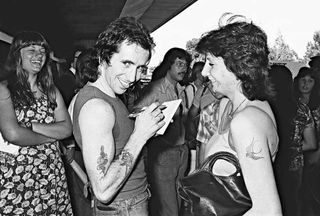 Bon Scott signs an autograph for a fan as the band returns to Sydney after an overseas tour, 26 November 1976.