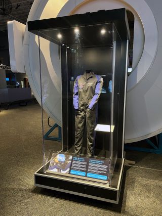 a museum display showing a black flight suit in a glass case.