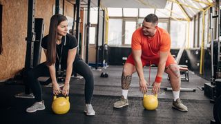 Man and woman train with kettlebells in a gym space