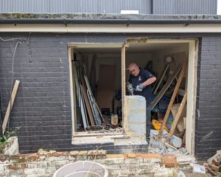 A male laborer inside garden outbuilding removing remove bricks and breezeblocks to make space for sliding door install