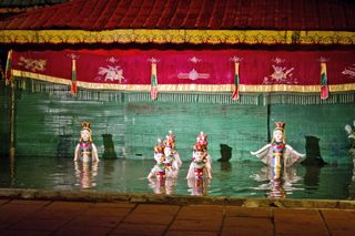 Elaborately dressed puppets dance on the water in a theater in Hanoi