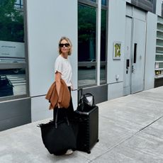 Stylist and fashion editor Natalie Cantell on her way to the airport wearing a neutral travel outfit with Celine sunglasses, Vuori sweatpants, aReplica Store cashmere sweater, H&M t-shirt, Adidas Sambas, Toteme T-Lock bag, Naghedi oversize tote, and an Away suitcase.