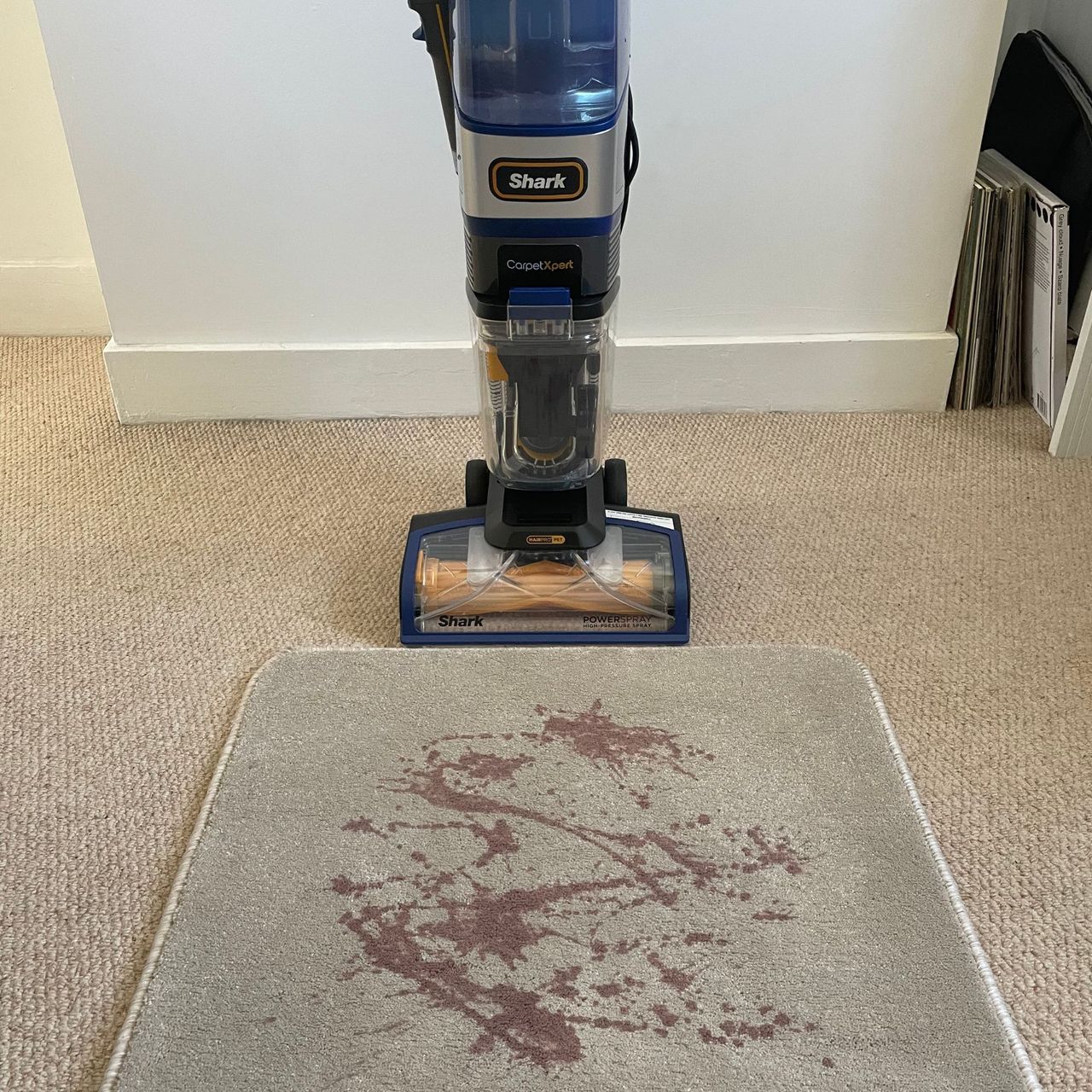 Red wine spilled on a carpet sample, with the Shark CarpetXpert HairPro Pet Deep Carpet Cleaner with Spot Cleaner EX250UK sitting behind it