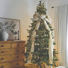 A bedroom with a lit-up Christmas tree decorated with a large off-white bow