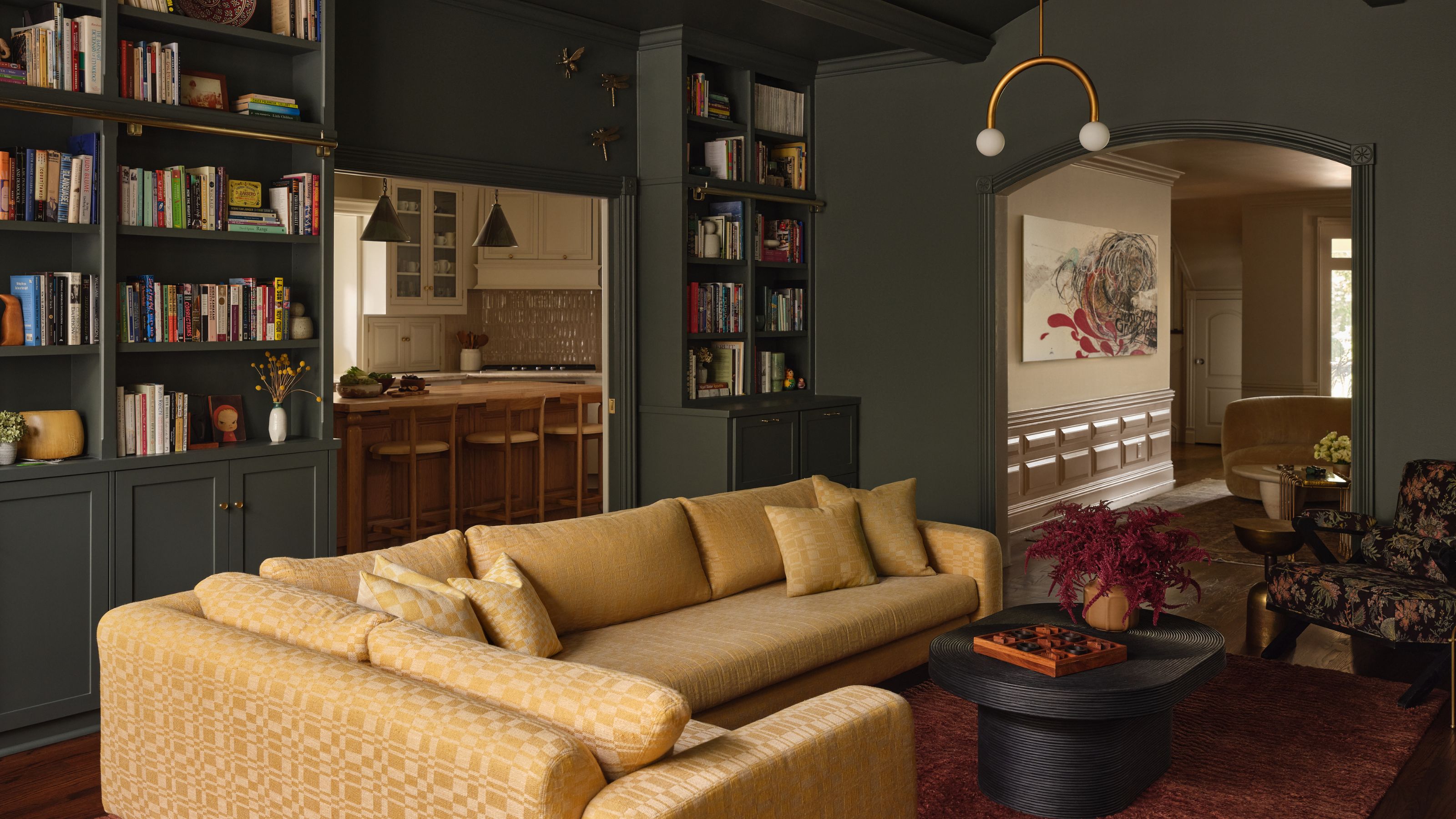 a dark green painted living room with yellow sofa, arched entry, and bookcases with storage