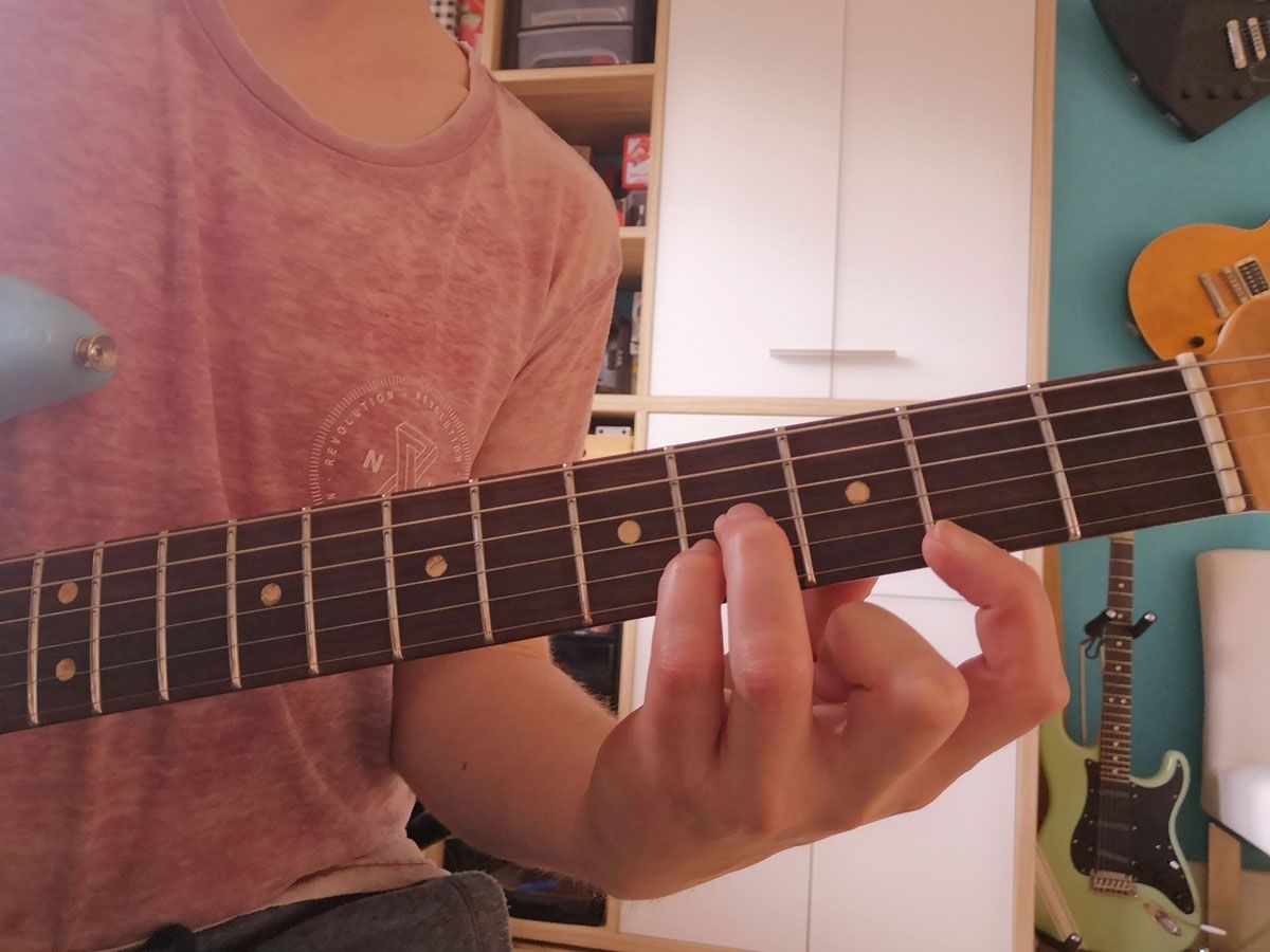 A person showing how to play part of a B major barre chord