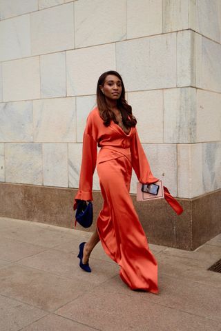 a woman wears an orange satin maxi dress with long sleeves