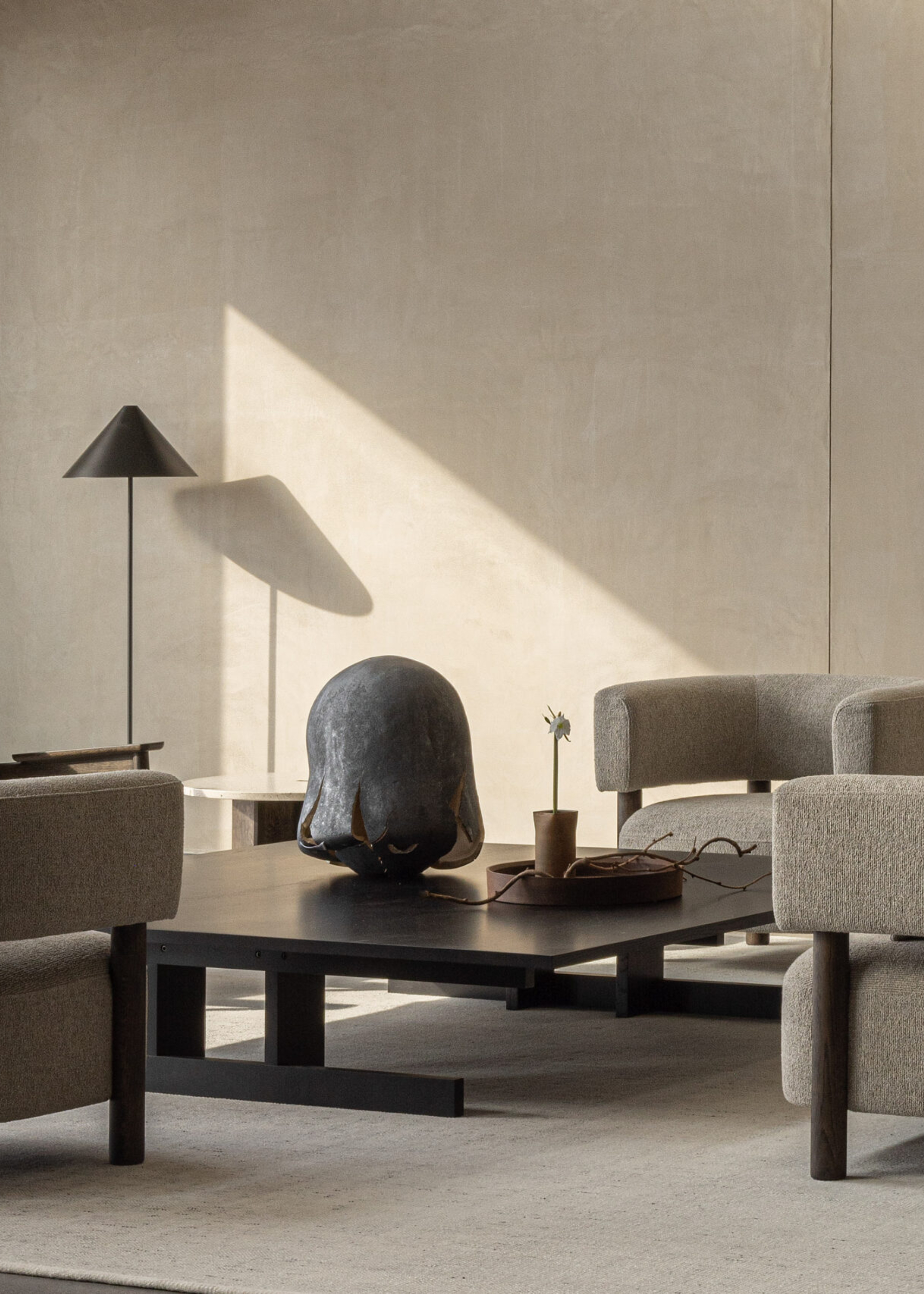 A wabi-sabi style living room with a black floor lamp, a black coffee table, and beige armchairs