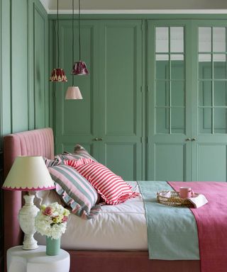 Green and pink bedroom with whimsical bedding, bedside table with lamp and flowers