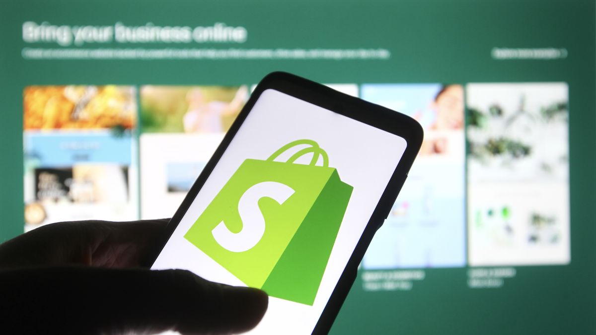 The Shopify logo on a smartphone in front of the background of the Shopify website