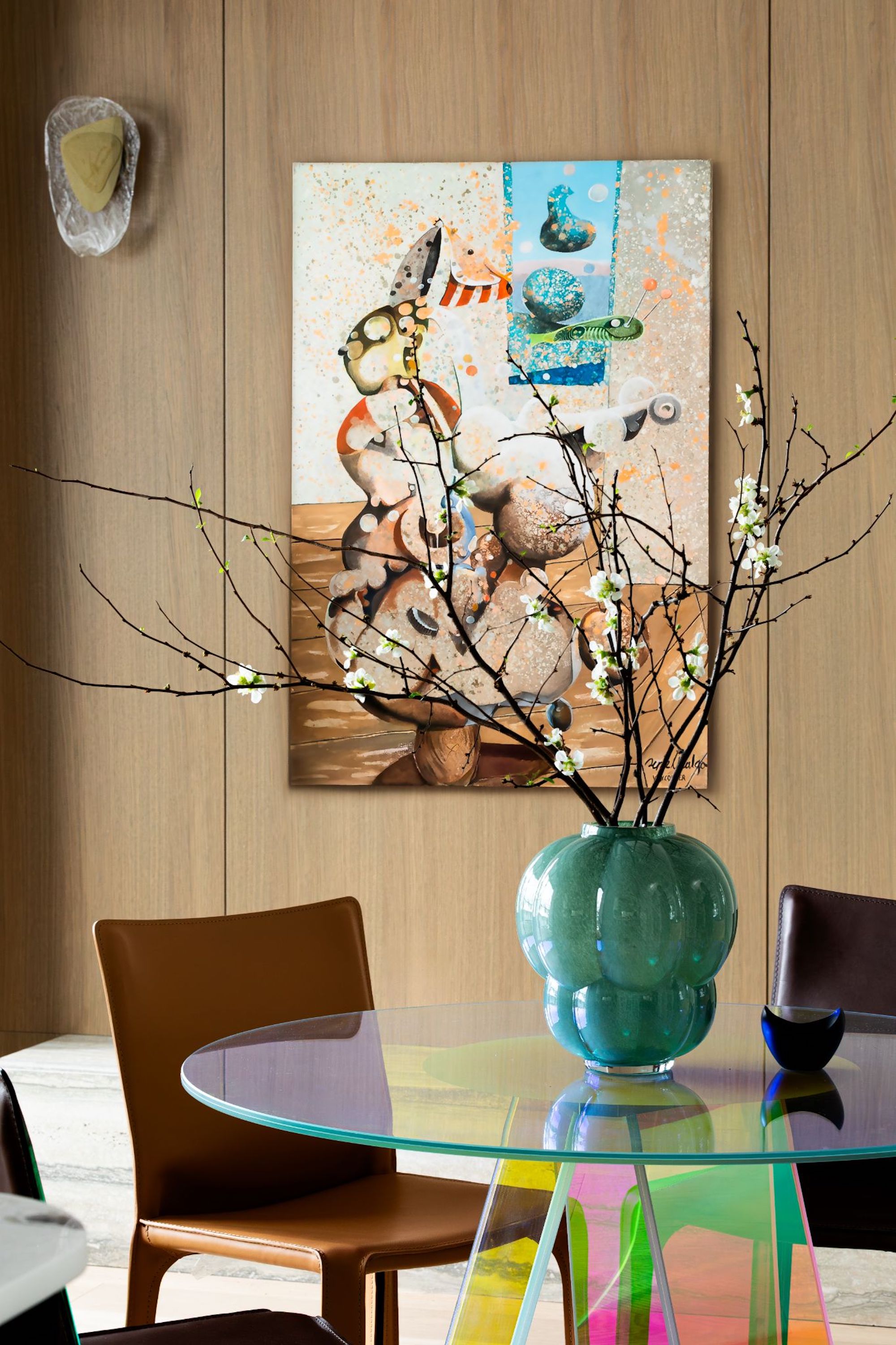 A dining area with an iridescent, round table and brown leather chairs around. Behind is a large surrealist artwork on the wooden clad walls.