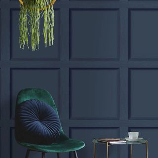 A wall covered in wallpaper representing 3D wooden panelling with a velvet chair and coffee table in front of it