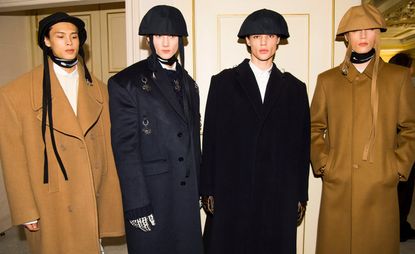 Four people in long coats stood in front of a closed doorway