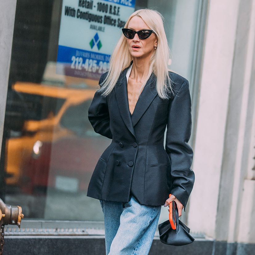 A woman wearing a black blazer, blue jeans, and black cat eye sunglasses