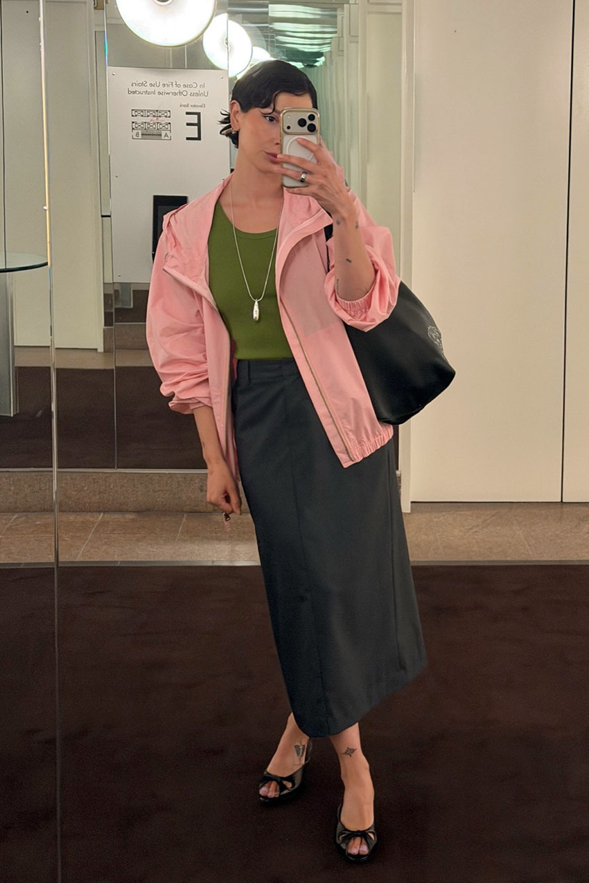 a woman wearing a pink jacket over a green tank top, a black long skirt, and black strappy peep toe heels