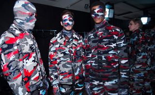 Male models in blue, grey, white and red camo outfits wearing camo face paint and balaclavas
