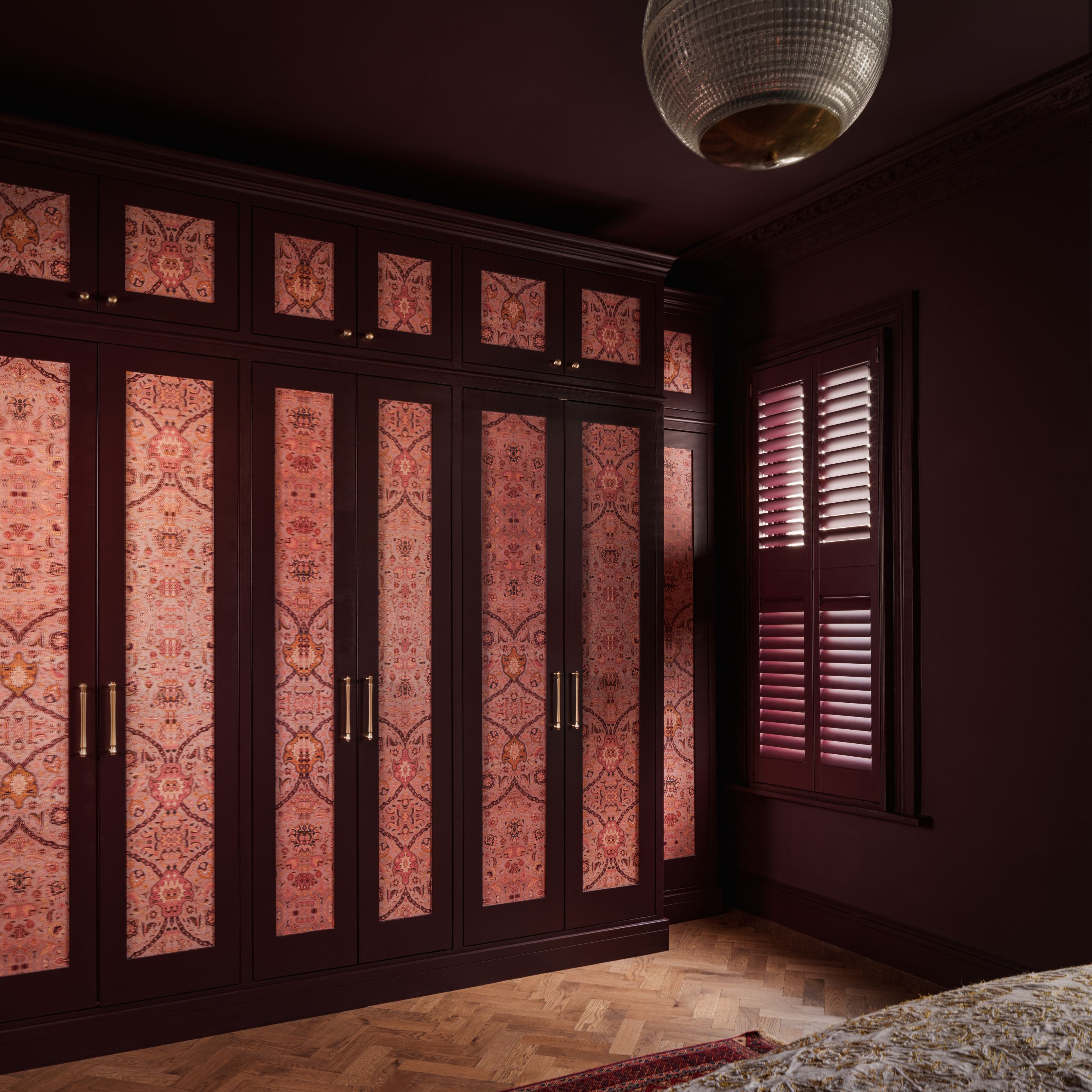 Built-in wardrobes in a modern burgundy bedroom with wallpaper in the inner paneling