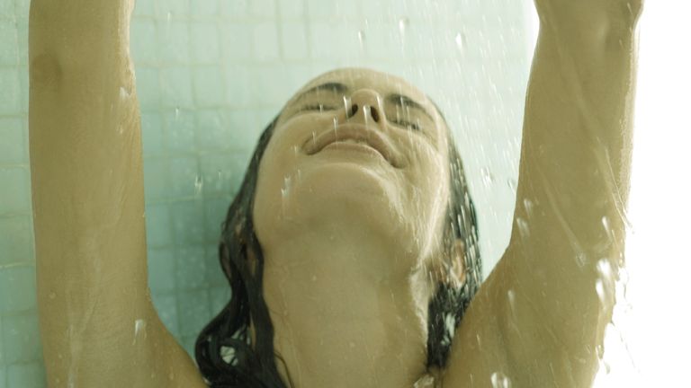 Woman in shower with arms up and head back