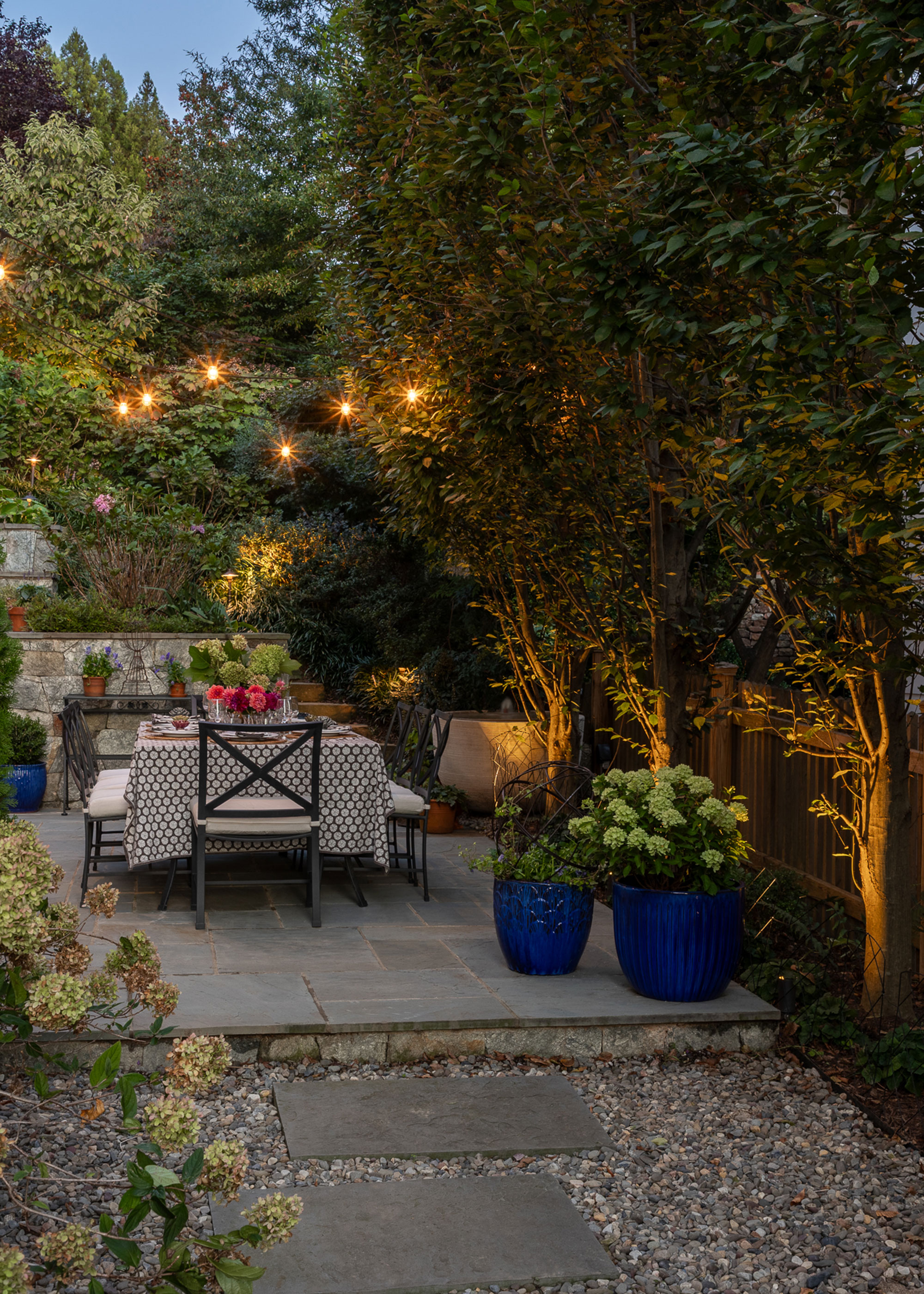 Outdoor dining area with uplit trees and exterior string lights