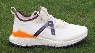 Cole Haan ZeroGrand Overtake Golf Shoe resting on the golf course showing off its excellent white and orange colorway