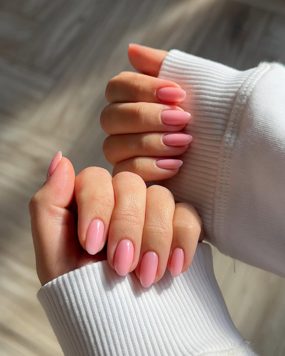 Close-up photo of a person&amp;rsquo;s hands showcasing a bubble gum pink manicure on almond nails.