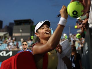 Emma Raducanu signs a ball as she leaves a tennis court