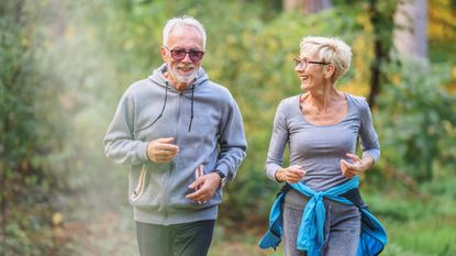 An older couple smiles while hiking through a wooded area.