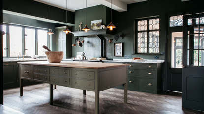 A spacious dark green kitchen in a traditional style with a slightly lighter green island and dark wood flooring
