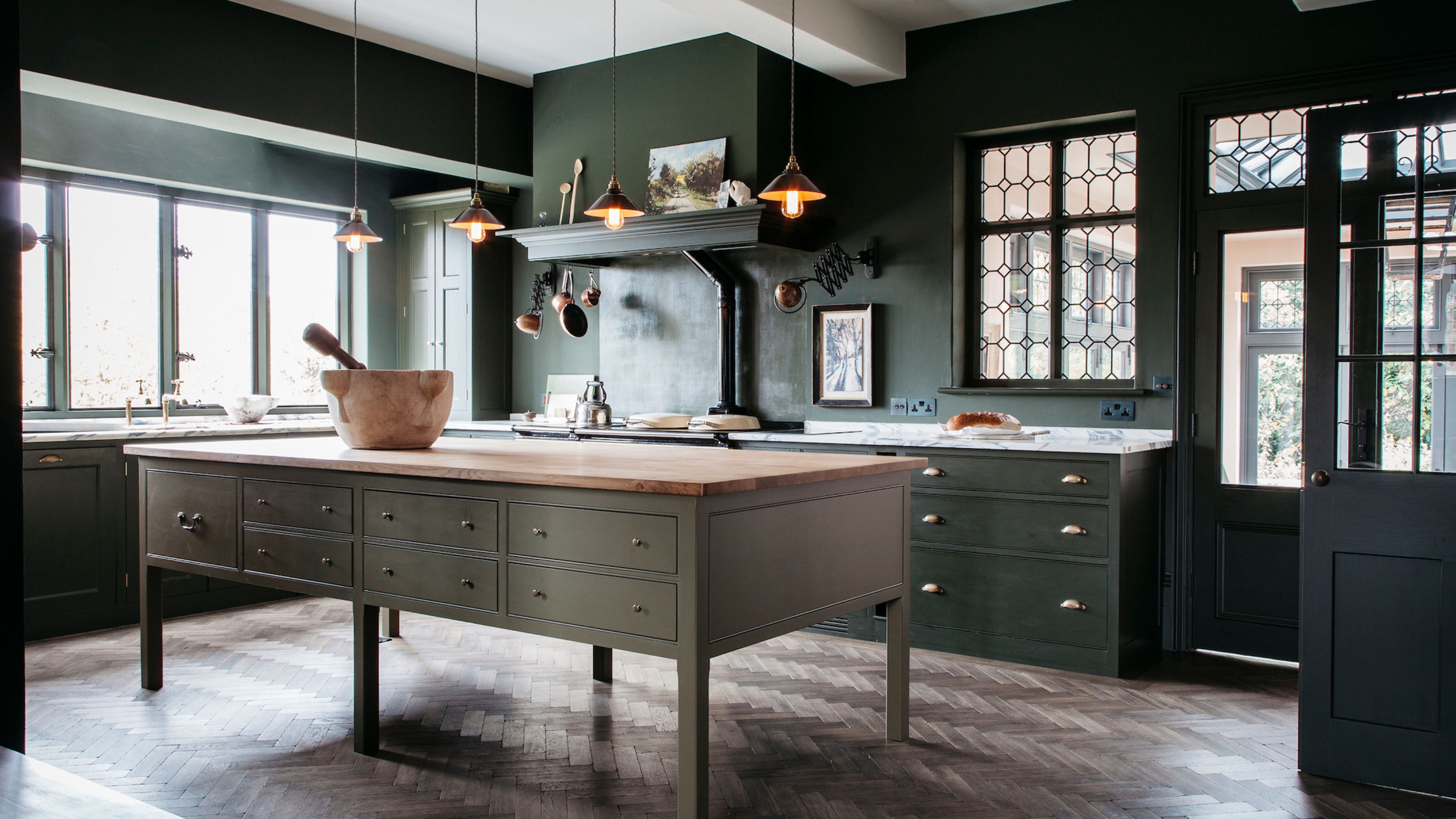 A spacious dark green kitchen in a traditional style with a slightly lighter green island and dark wood flooring