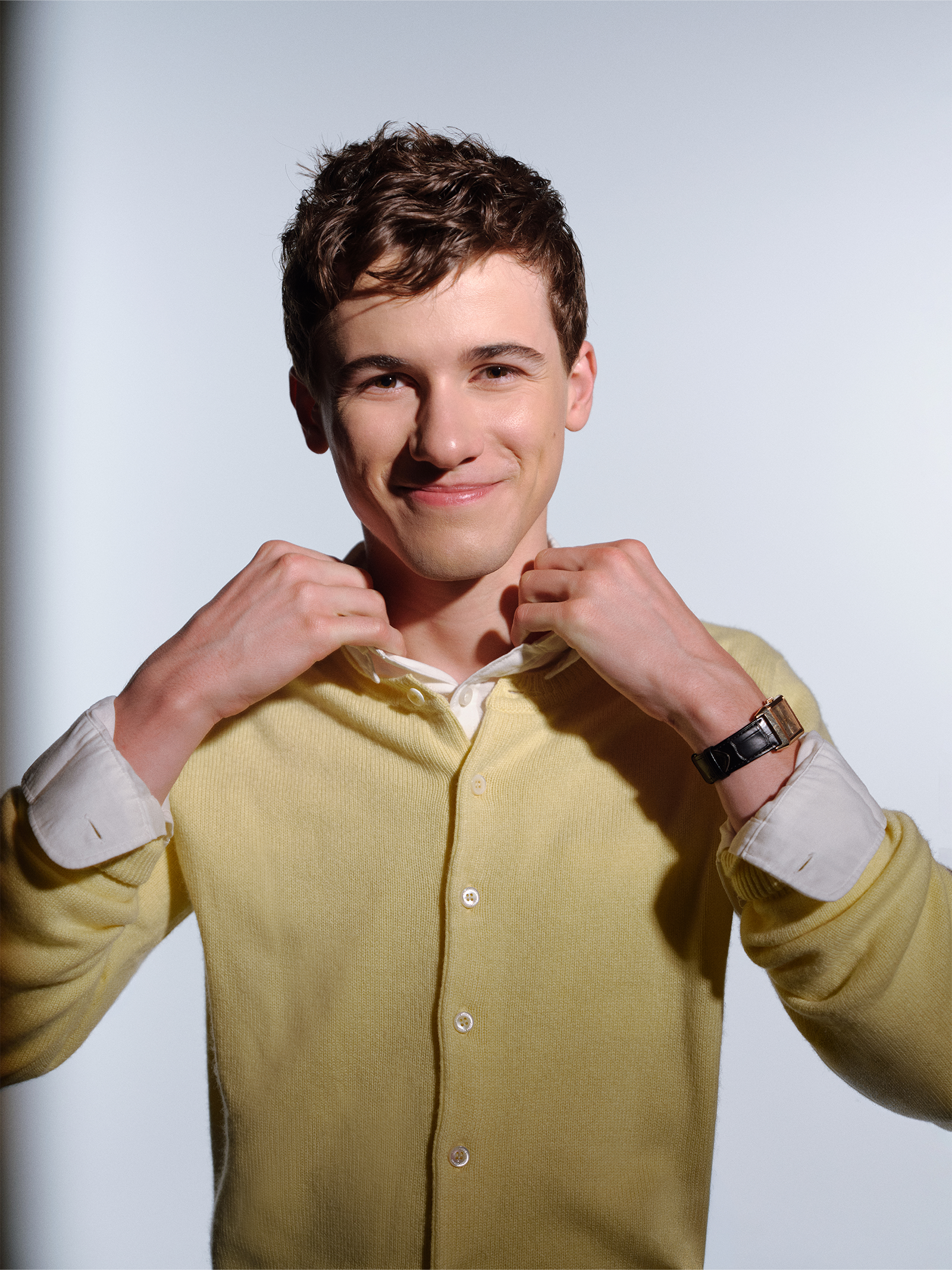 Actor Sam Nivola, photographed by JJ Geiger for Who What Wear. He is wearing a white button-down shirt and khaki trousers with a yellow cardigan.