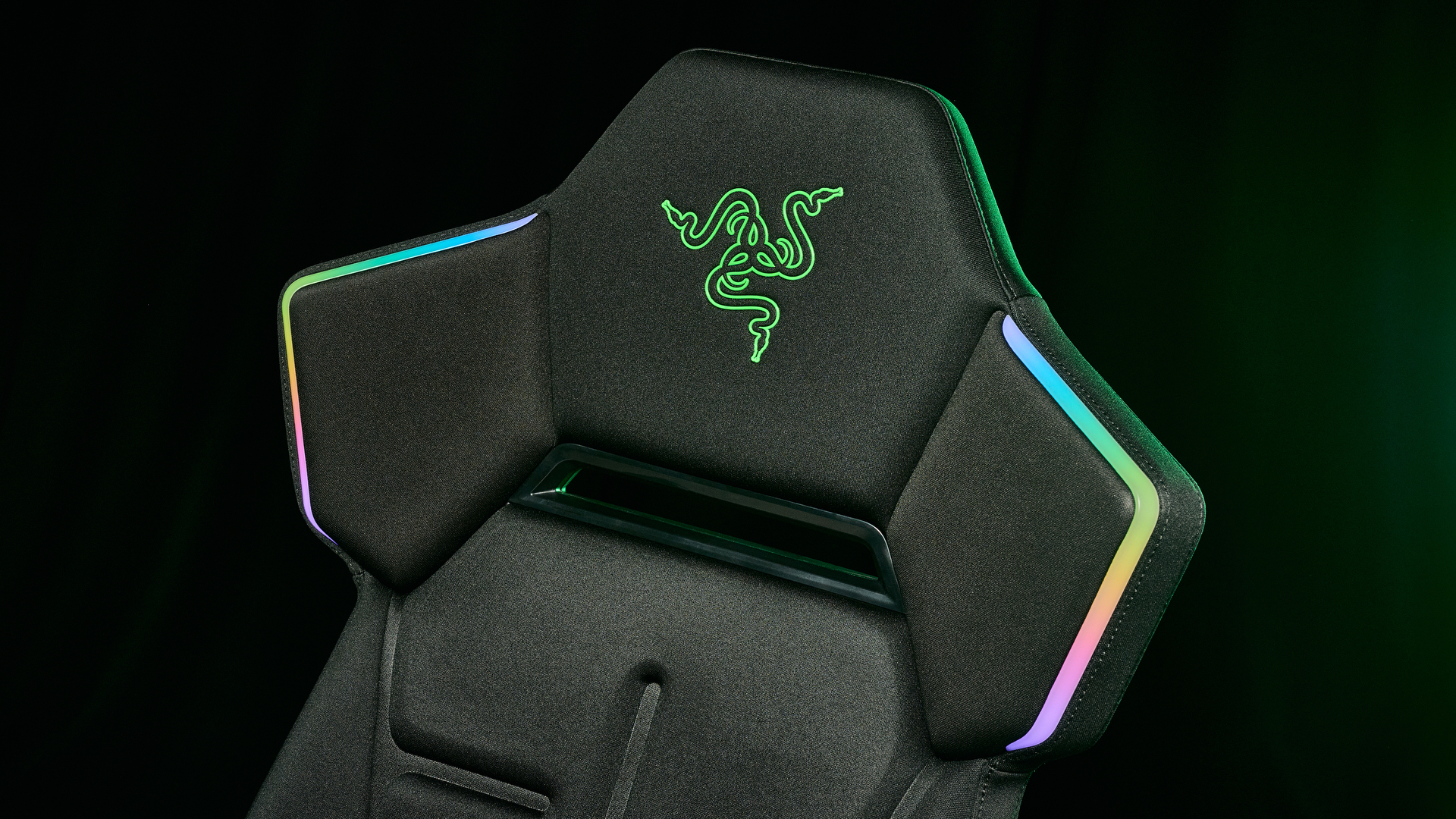 The Razer Soma Chroma chair in an industrial setting head rest with the RGB on and the Razer logo showing, illuminated with a green glow