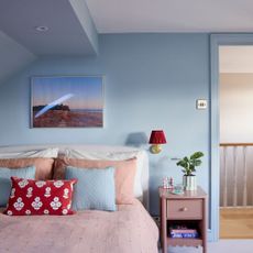 Blue painted bedroom with pink bedding and a pink side table next to it