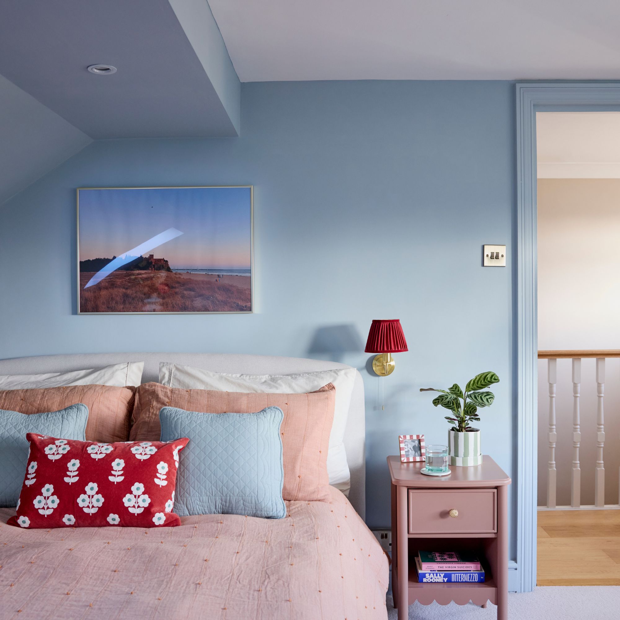 Blue painted bedroom with pink bedding and a pink side table next to it