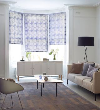 Blue patterned roller blinds on bay windows in white living room with accent floor lamp