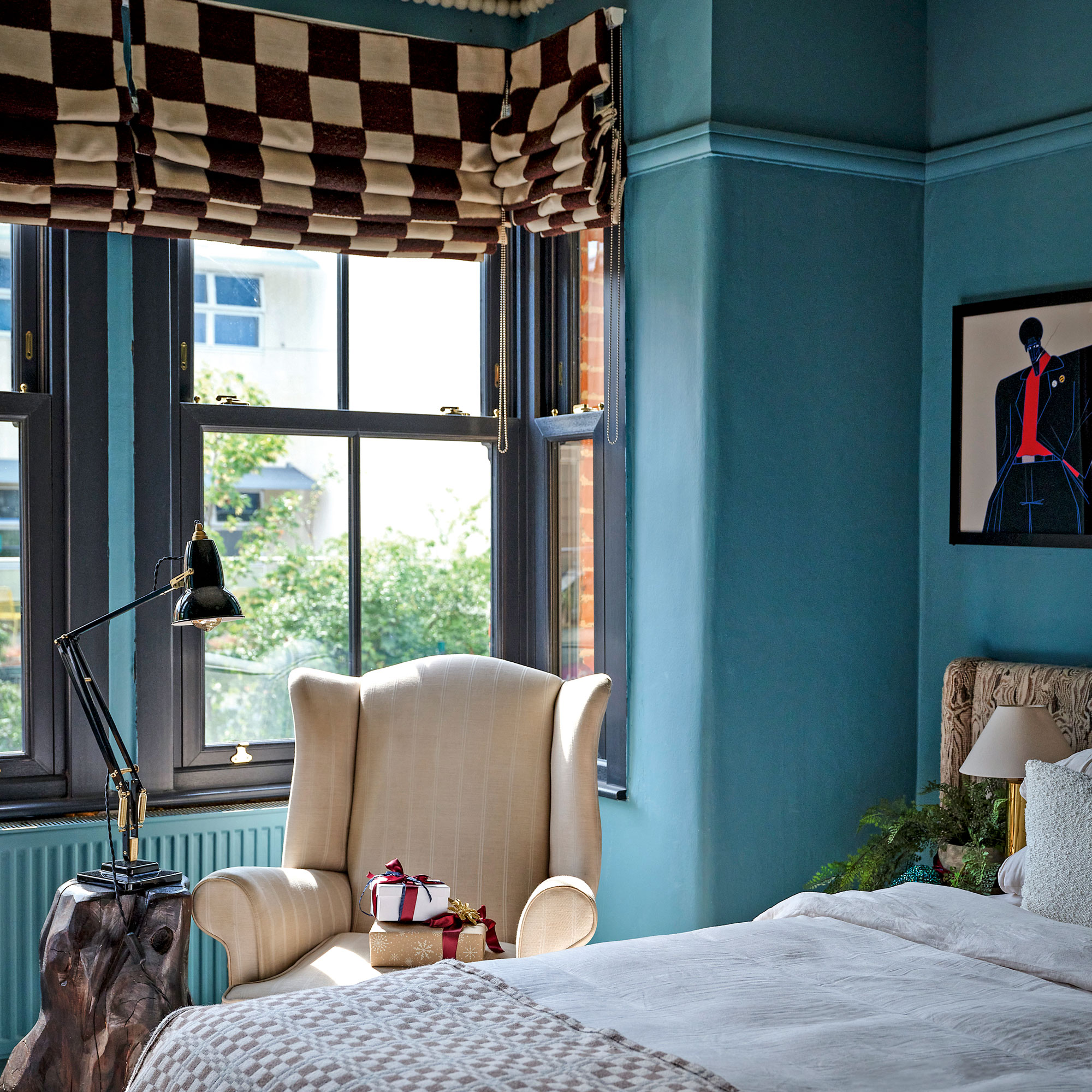 Blue bedroom with chequered roman blind, cream wingbacked chair and black lamp