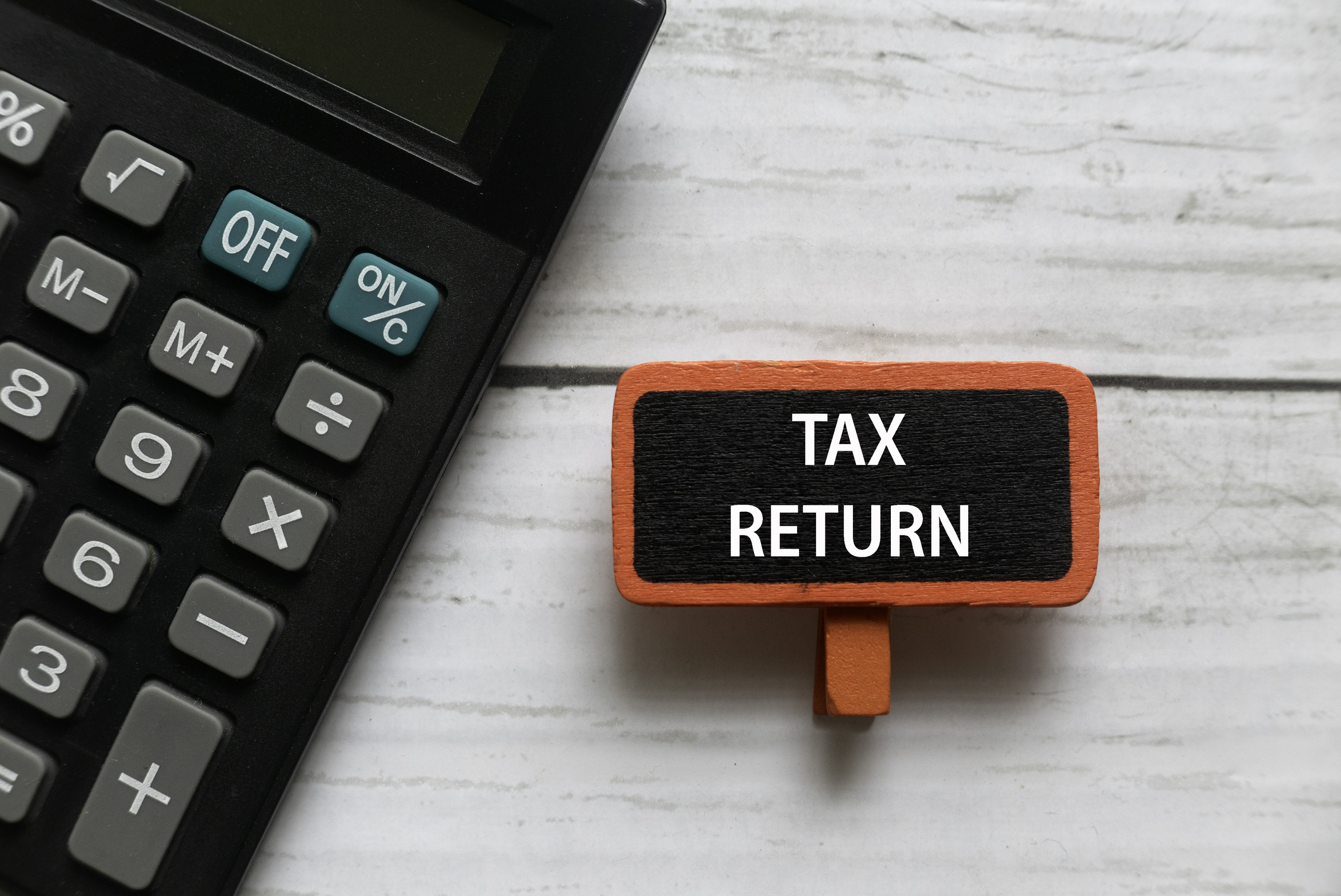 Top view of calculator and red tag written with TAX RETURN on white wooden background.