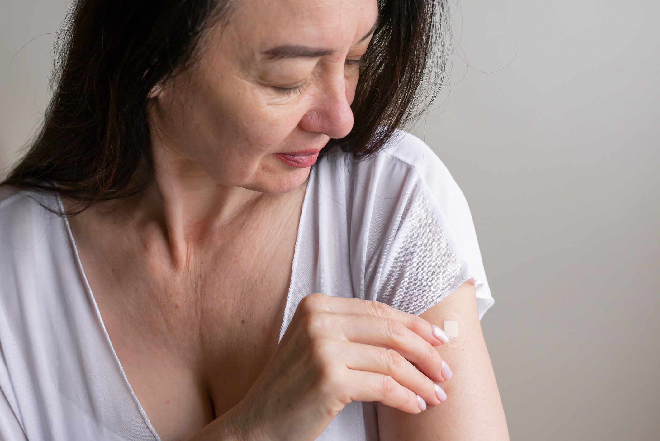 Жена тамне косе у белој мајици ставља фластер на леву руку.