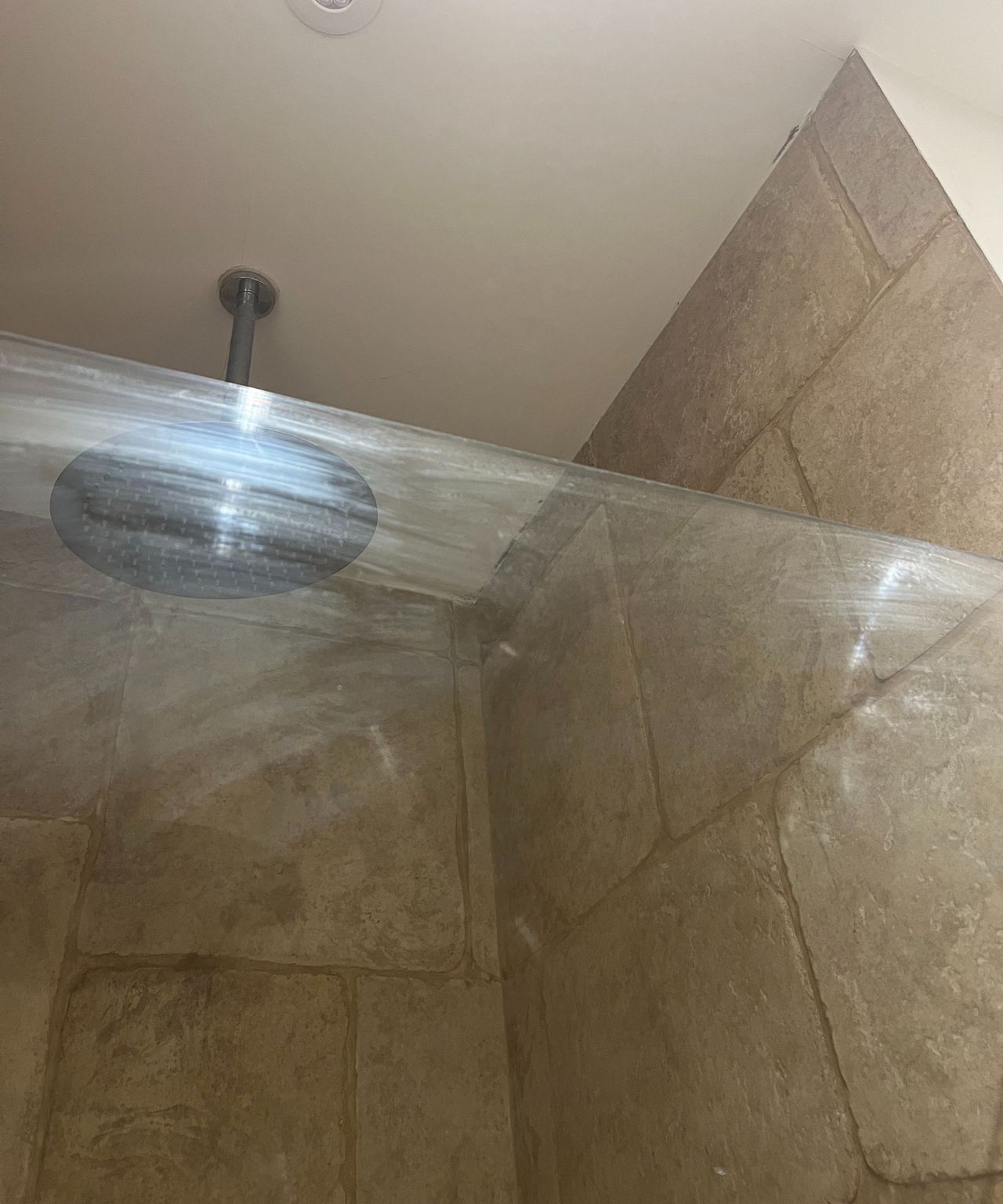 A smudged shower screen with large beige tiles behind