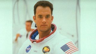 a man in a helmetless spacesuit stares into the camera. he is in a white room.