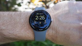 En Google Pixel Watch med ett blågrått armband runt en handled.