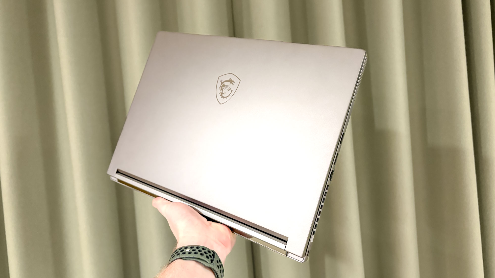 MSI Creator A16 AI+closed in hand with green curtain in background