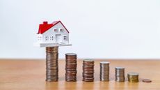 A small model house sitting on top of a stack of coins. 
