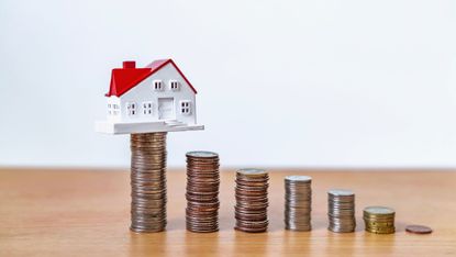 A small model house sitting on top of a stack of coins.
