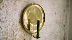 Pooky's Bellamy Candle Sconce styled with a lit moss green taper candle against a textured exterior wall